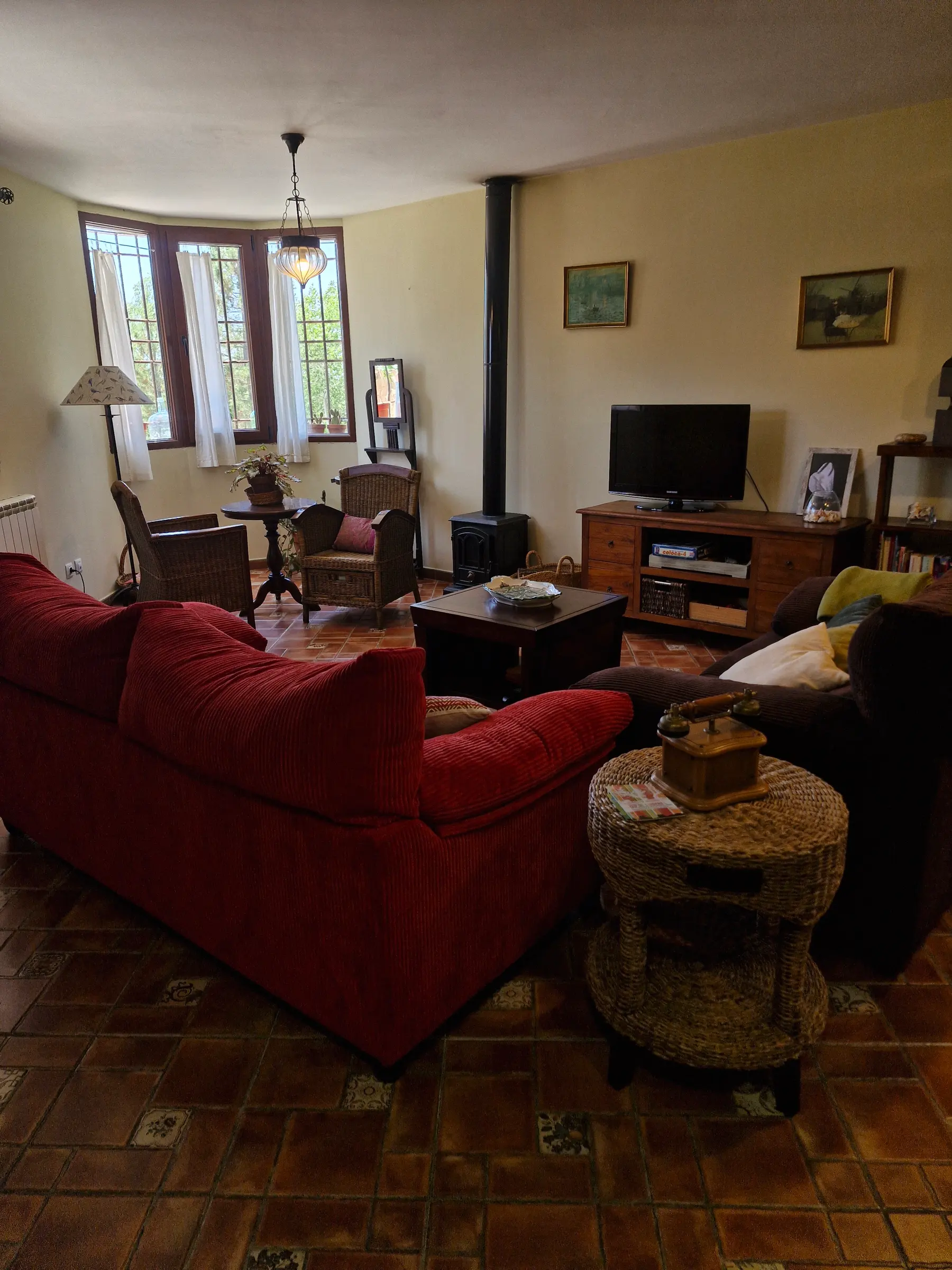 Salón de El Jardín con sofás rojos, estufa de leña y butacas de mimbre