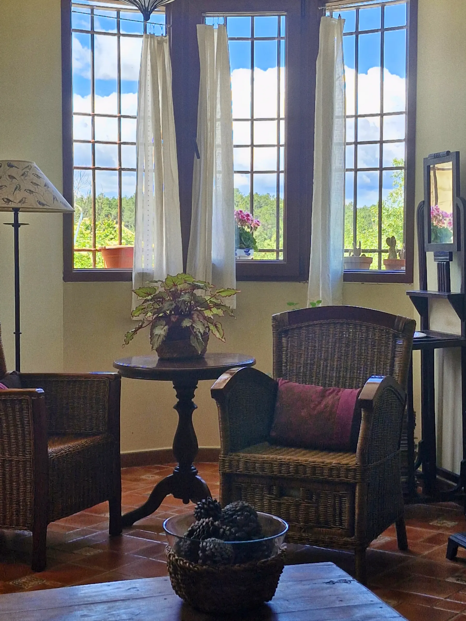 Rincón de estar de El Jardín con butacas de mimbre y velador junto a las ventanas