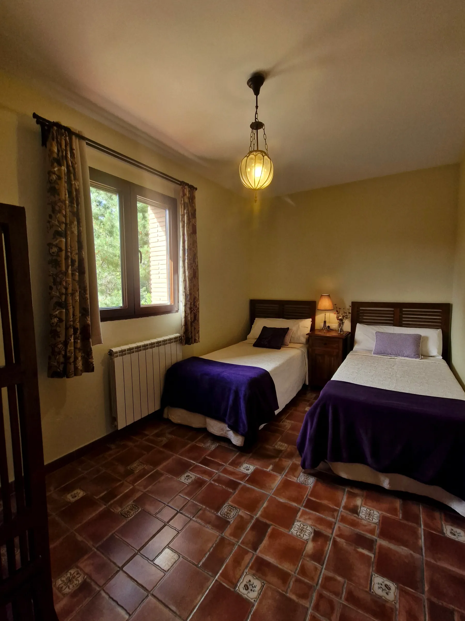 Dormitorio doble de El Mirador con colcha malva y lámpara de techo